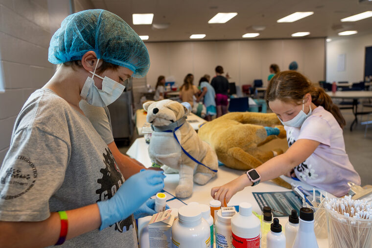 Two children learning veterinary skills by practicing administrating pretend medicine to a stuffed animal dog